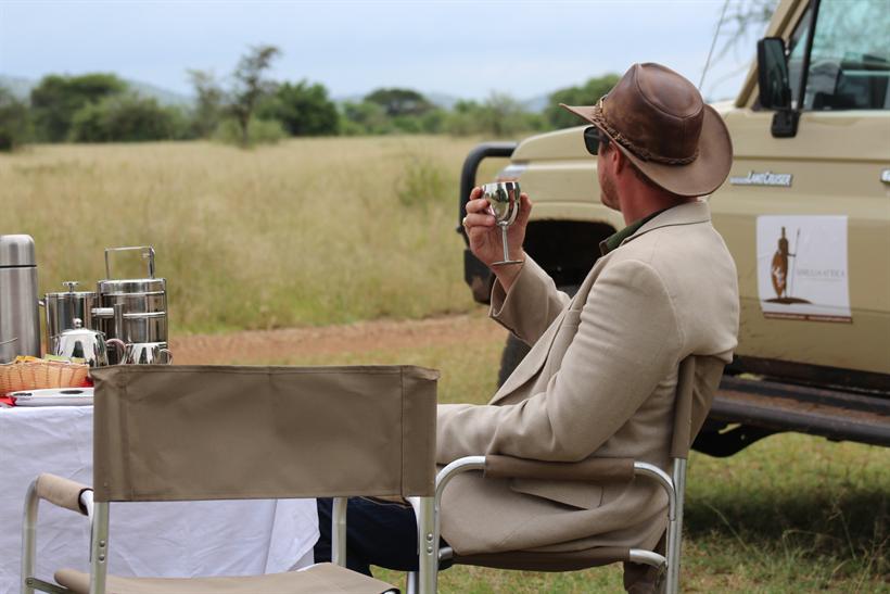 A guest raises a cup beside a Simulia Africa Land Cruiser